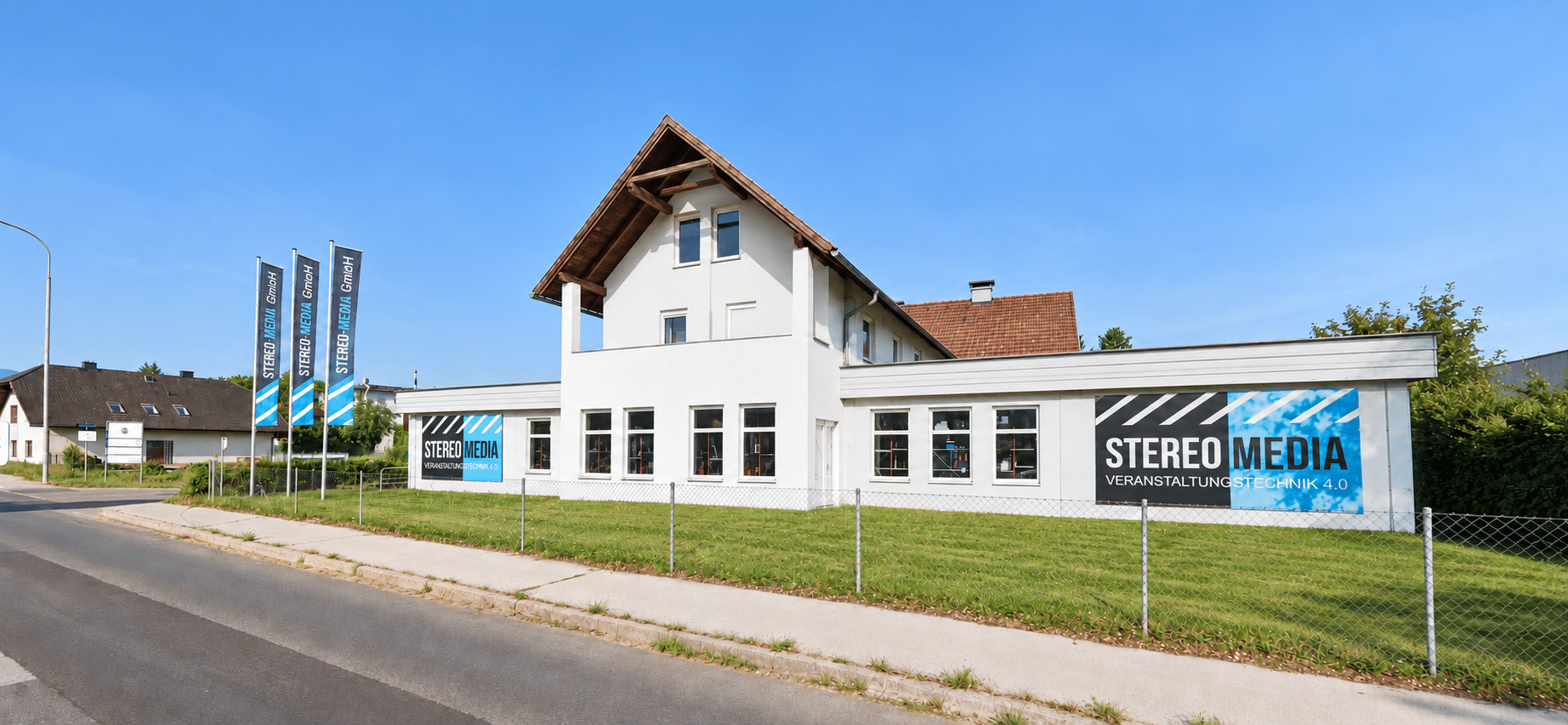 KI-bearbeitete Außenansicht des STEREO-MEDIA GmbH Firmengebäudes in Klagenfurt mit drei Fahnenmasten